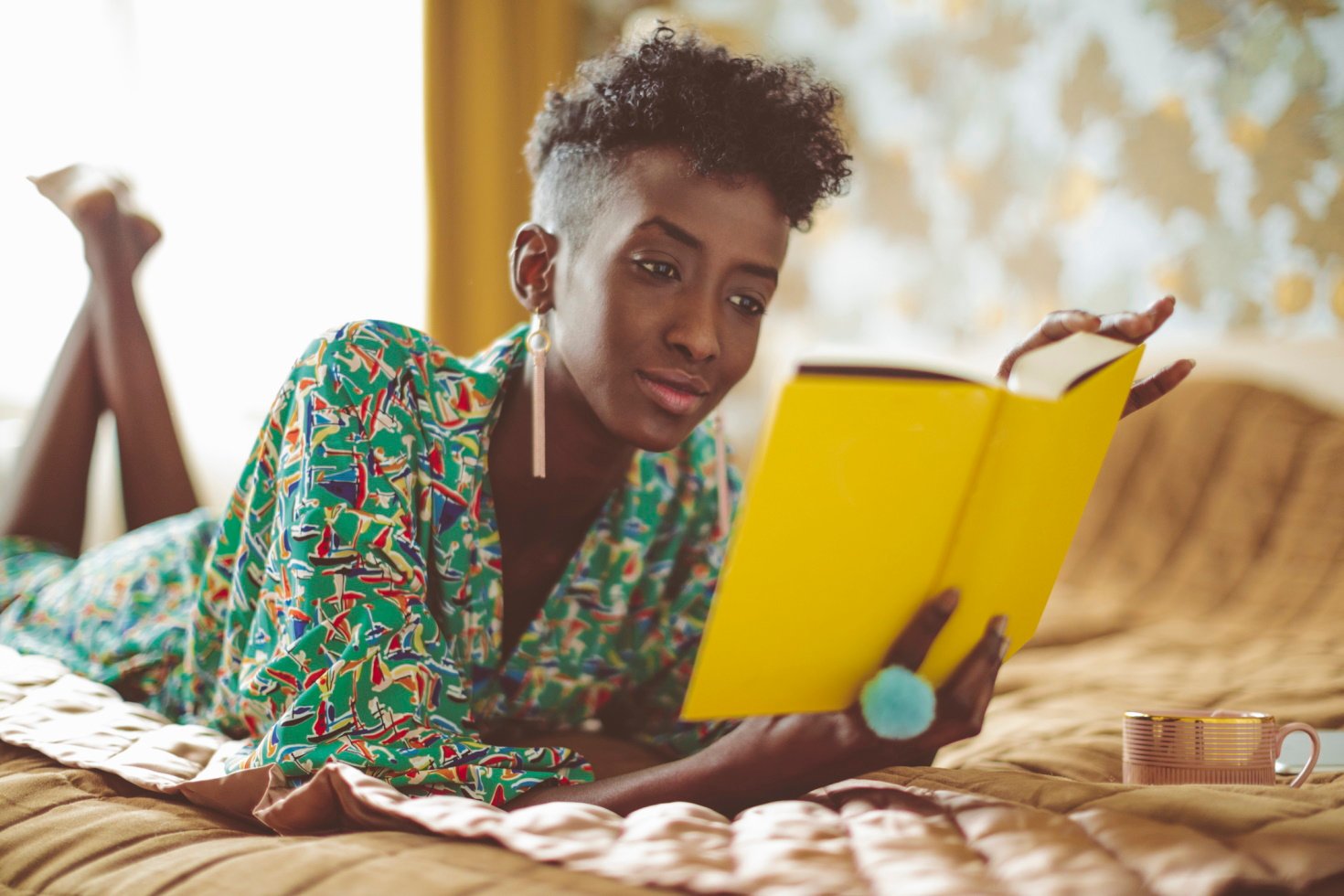 A stylish young woman reads a book while lying on her bed