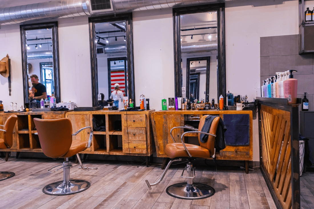 The interior of a salon features rustic wooden counter space, leather chairs, and tall mirrors.