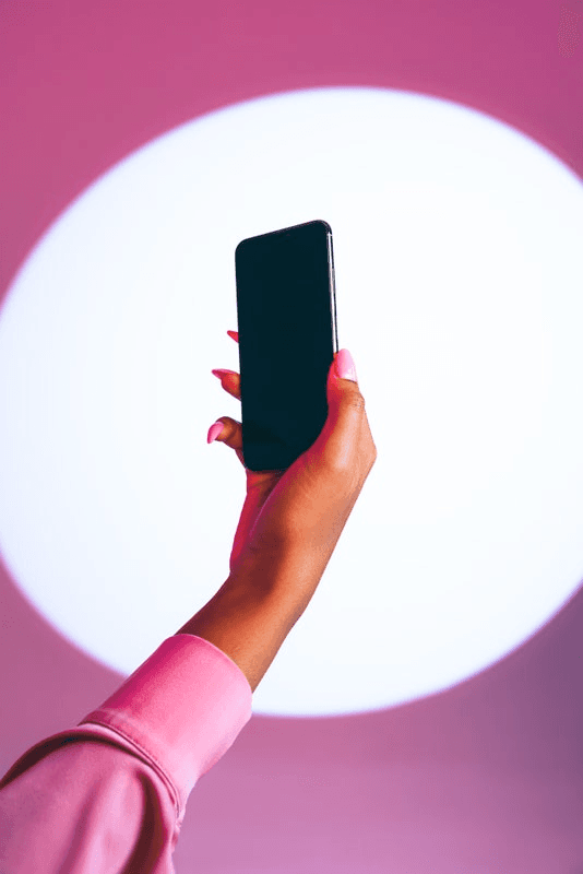 A hand with perfectly manicured nails holds up a smartphone.