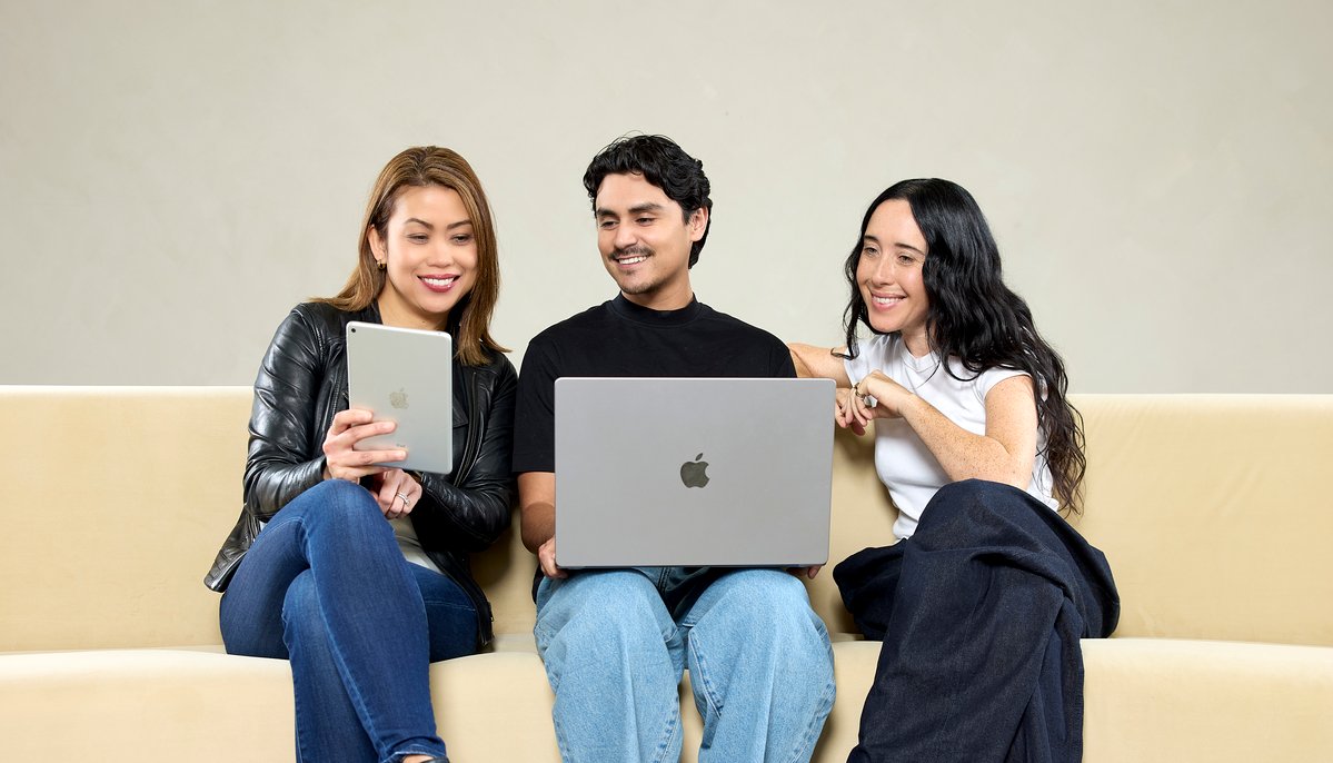 Three self-care business professionals sit on a couch looking at a tablet and laptop.