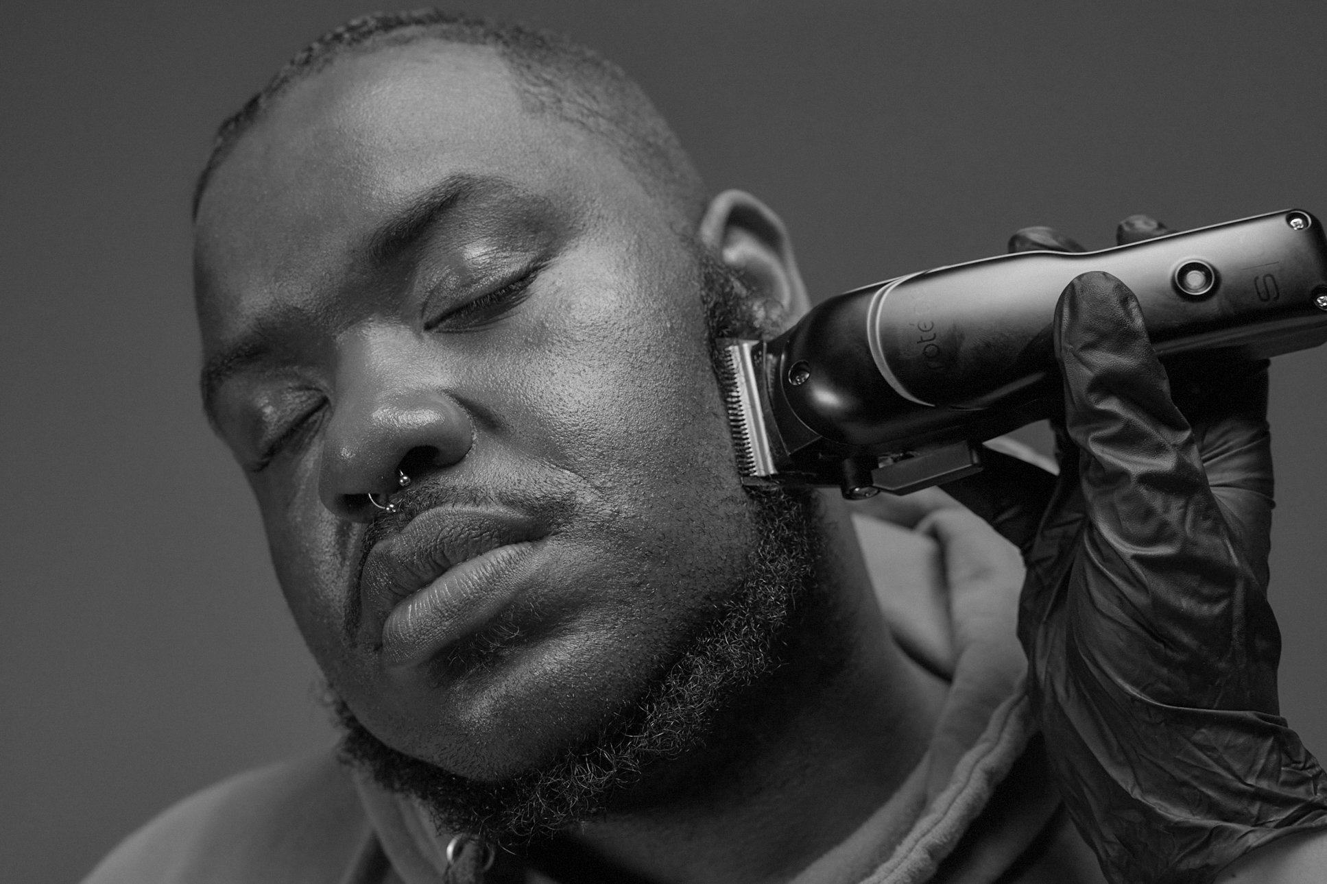 A black and white photo of a man having his beard shaved with an electric razor.