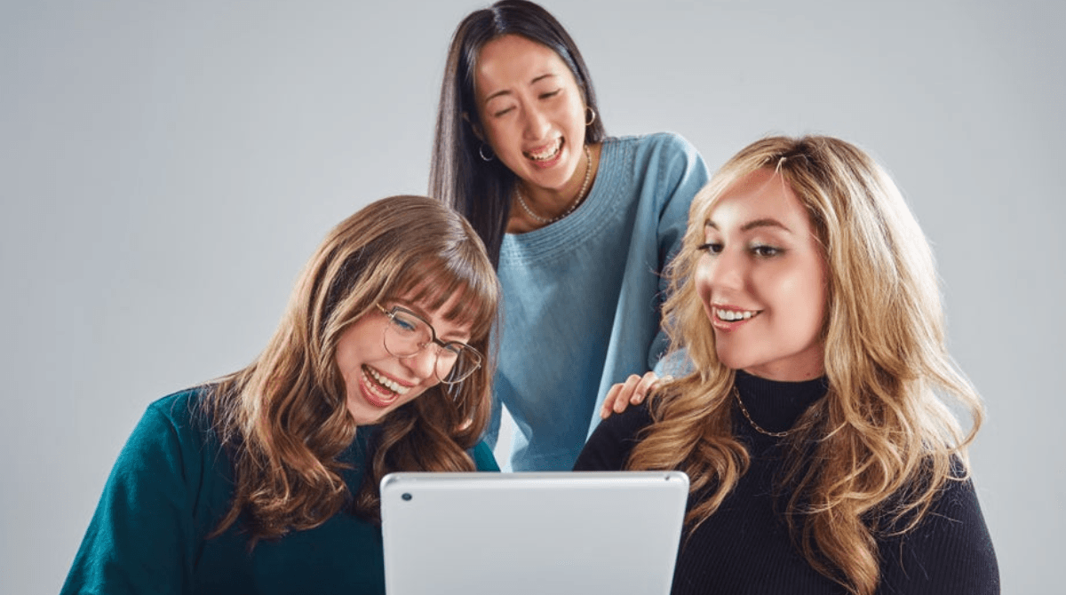 Three women smile while looking at an iPad screen.