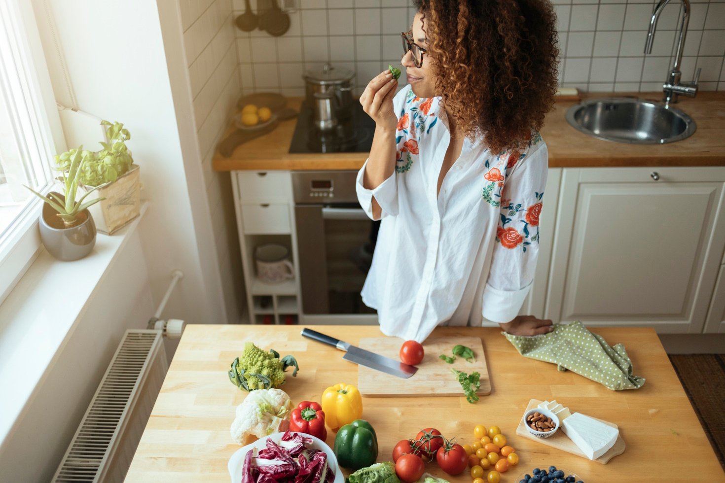 Woman snacking on broccoli floret while preparing a healthy meal in the kitchen.