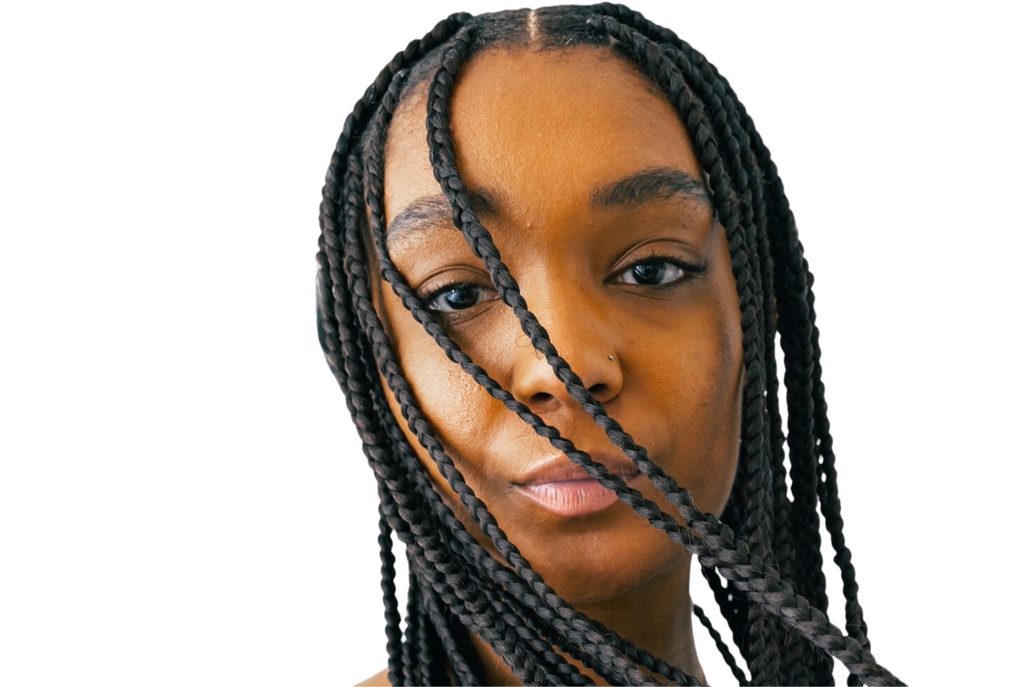 A woman with braids sweeping across her face stares into the lens of the camera.