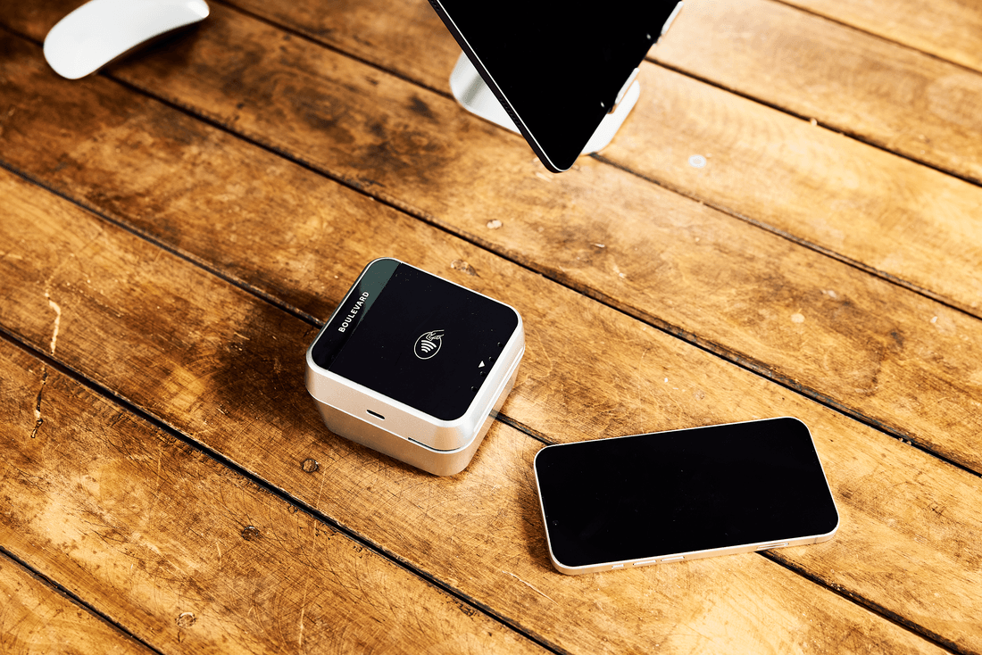 A wireless tap-to-pay station and smartphone rest on top of a wood desk in the waiting room of a medspa.