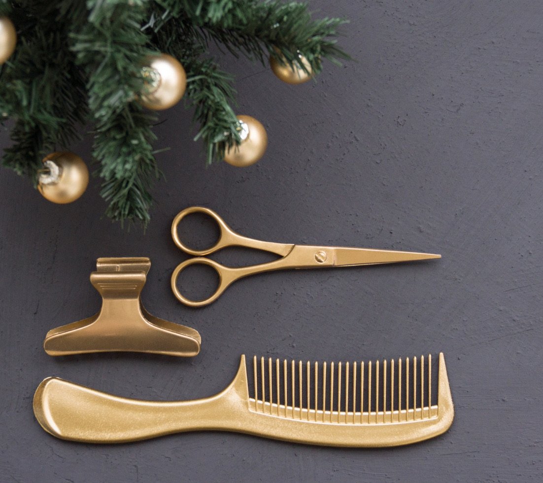 A gold comb, hair clip, and pair of scissors rest under the decorated branches of a fir tree.