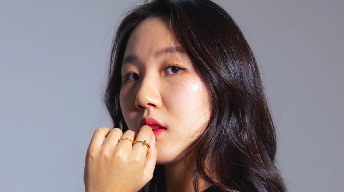 A woman with crossed arms and red lipstick glances at the camera.