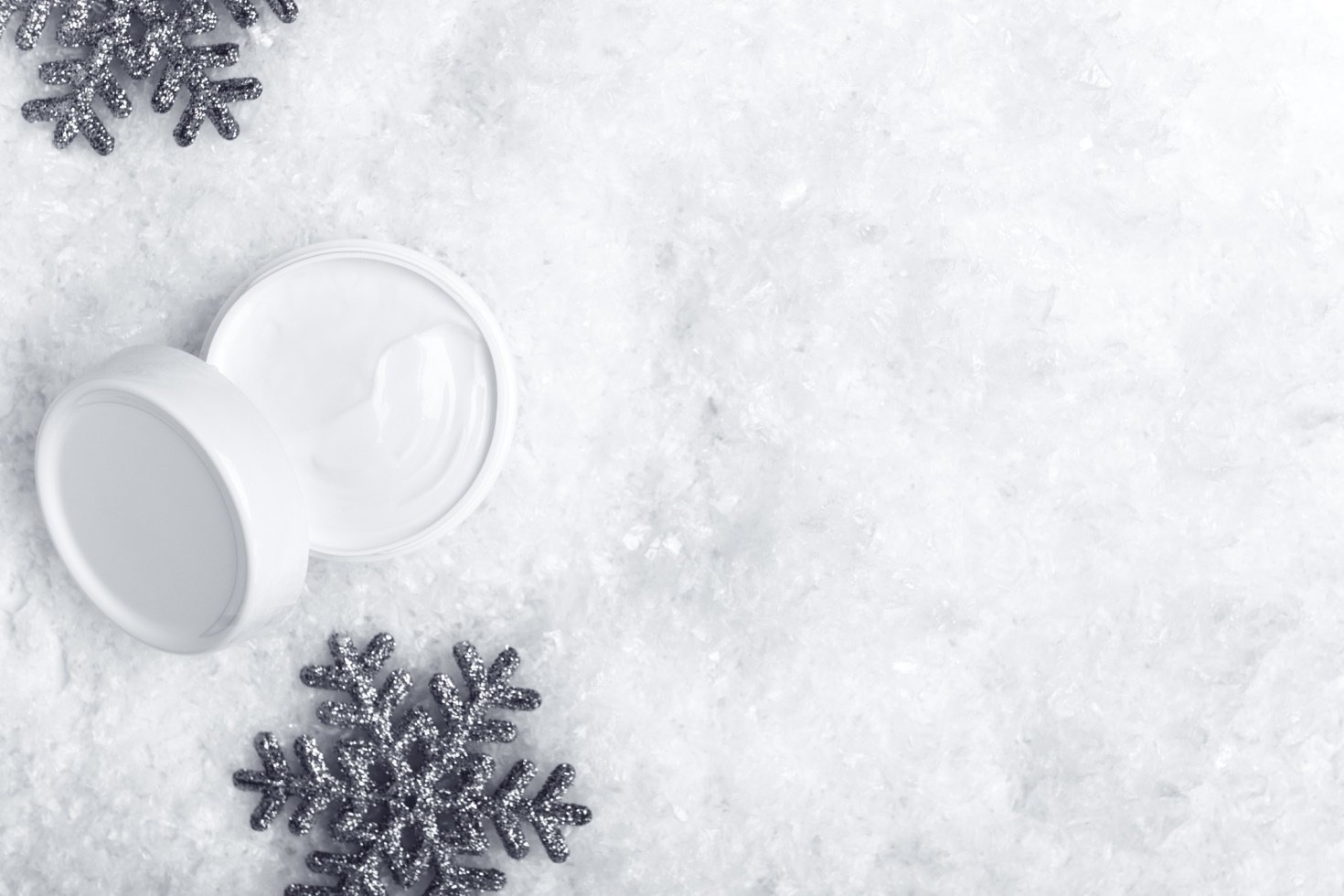 Open jar of cream on icy background with snowflake ornaments