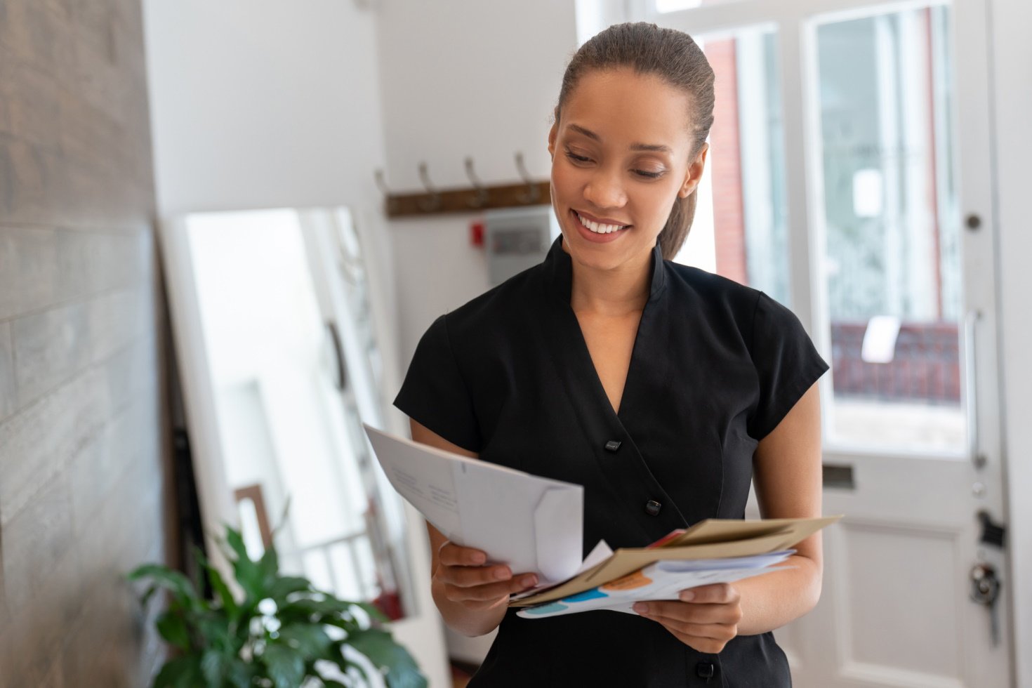 A women stands in her salon and looks down at documents in her hands while smiling.