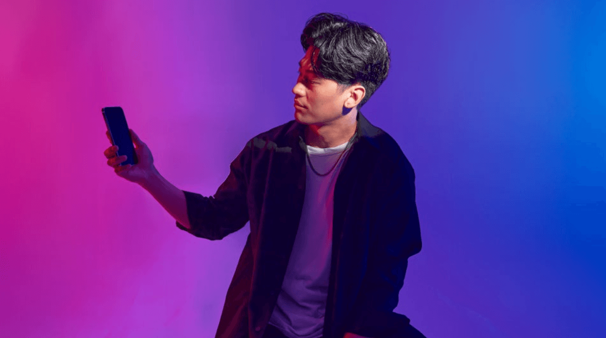 A man checks a smartphone while sitting on a stool.