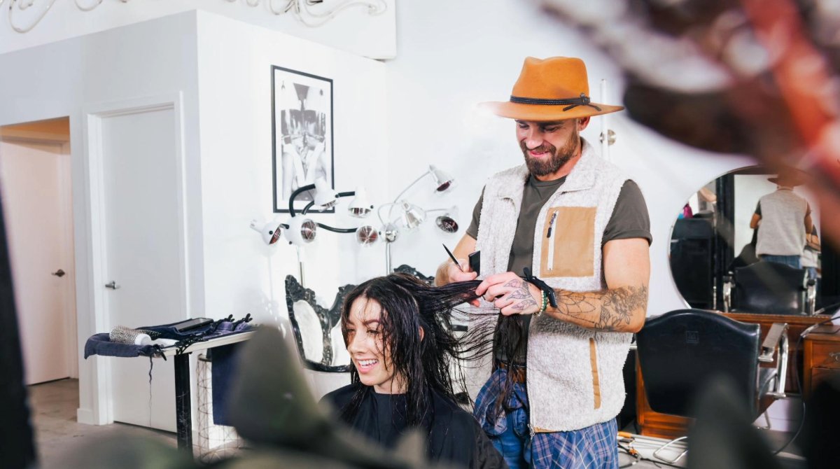 A hairstylist cuts a woman's black medium-length hair in a modern salon.