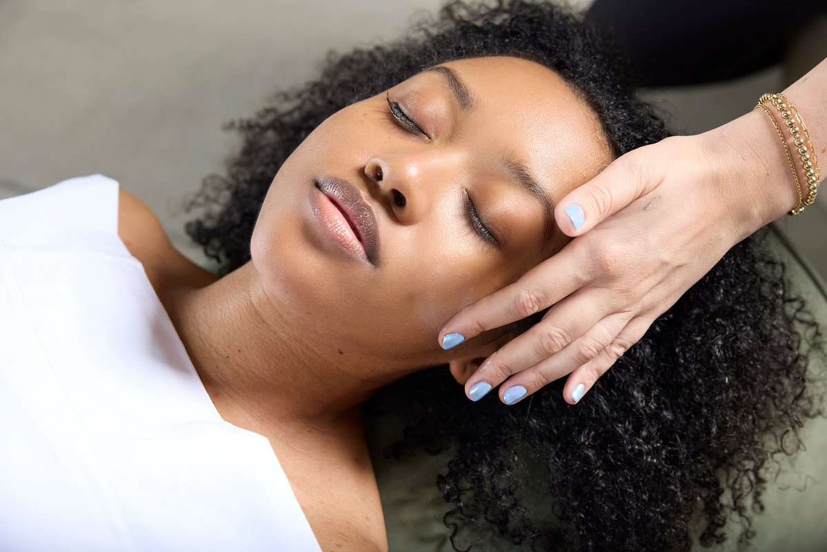A woman laying on a massage table receives a head massage.